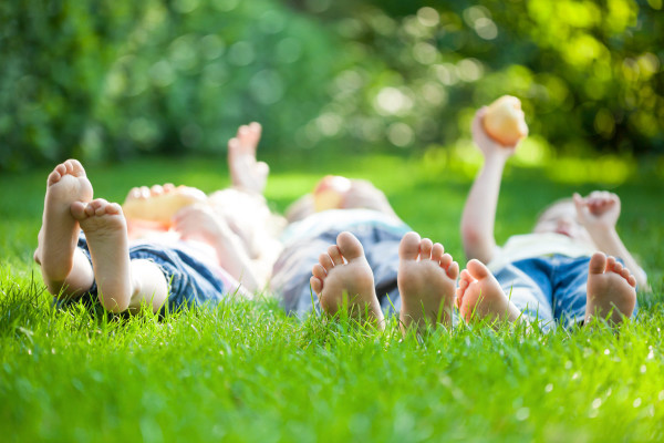 Three children laying barefoot in the grass.