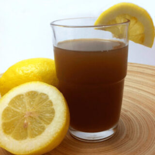Glass of homemade iced tea with lemon slices on a wooden platter.