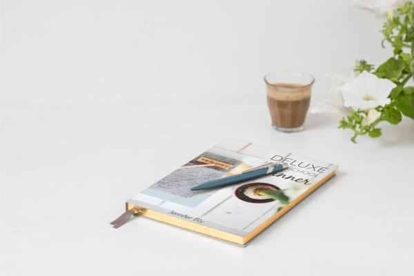 Book bound homeschool planner on a table with a pen, chocolate milk, and white flowers