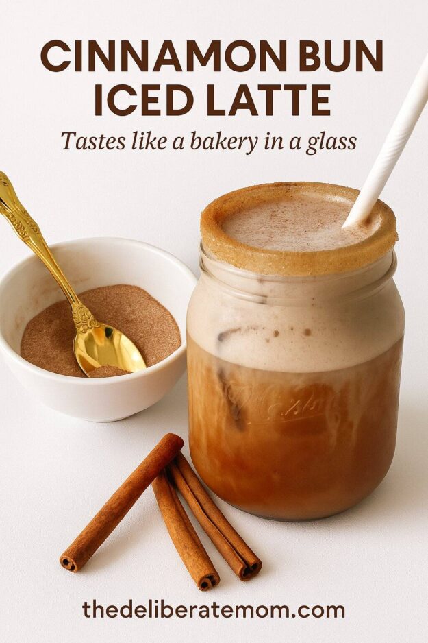 Cinnamon Bun Iced Latte in a mason bar glass with a white straw. White bowl of cinnamon sugar with a gold spoon to the left of the drink.